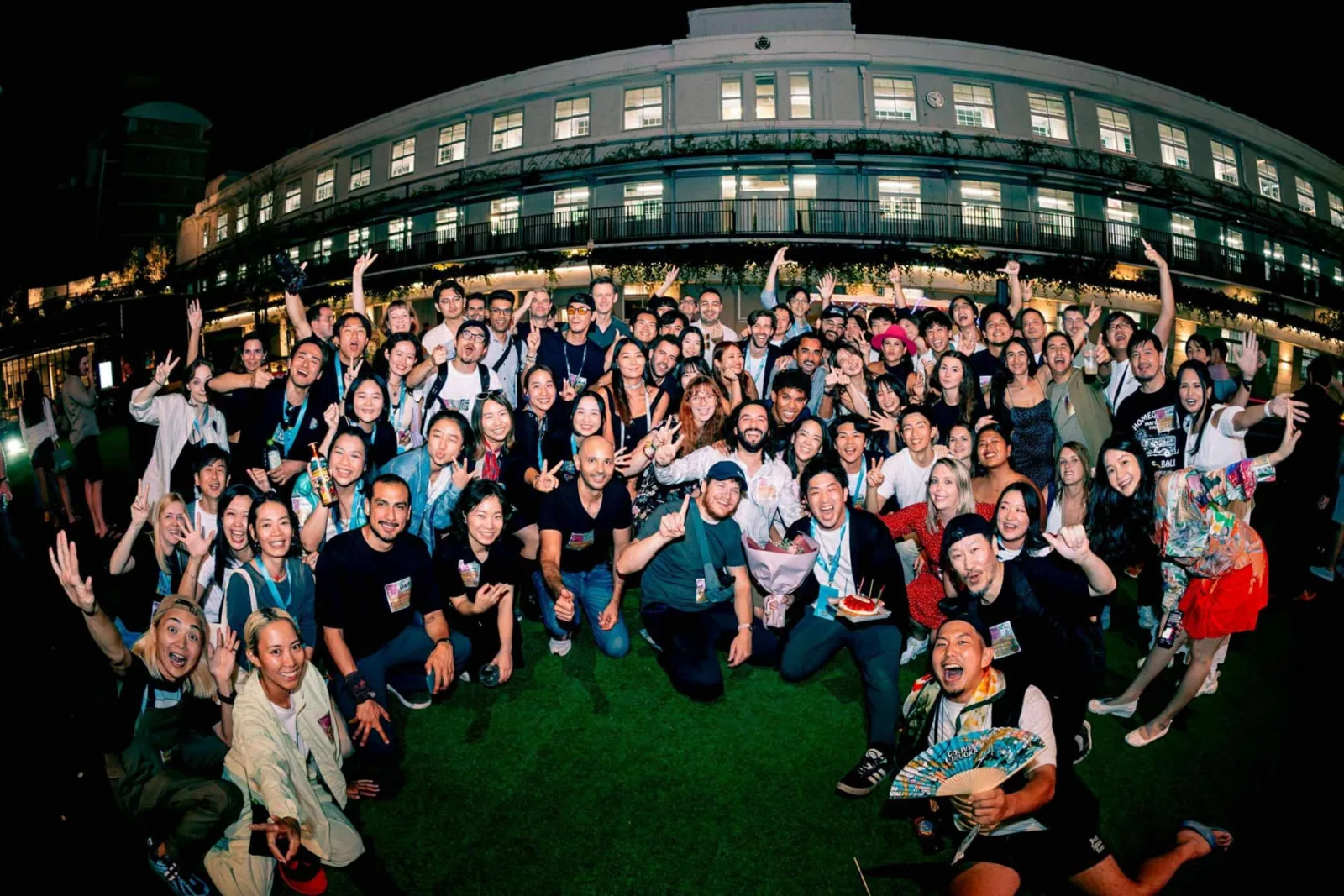 Colive Fukuoka participants celebrating together at night on a lawn in front of a lit-up historic building.