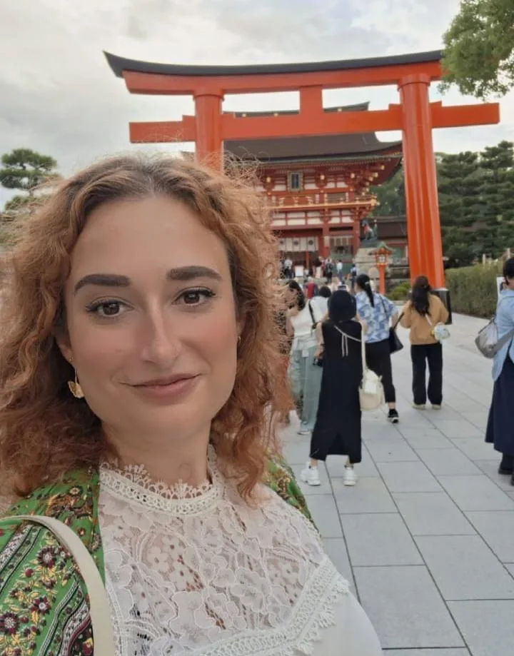 Mirela Curiman standing in front of a traditional red torii gate at a Japanese shrine.