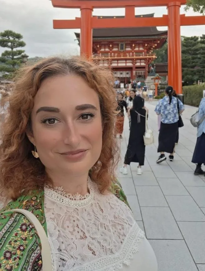 Mirela Curiman standing in front of a large red torii gate at a shrine in Kyoto, Japan.